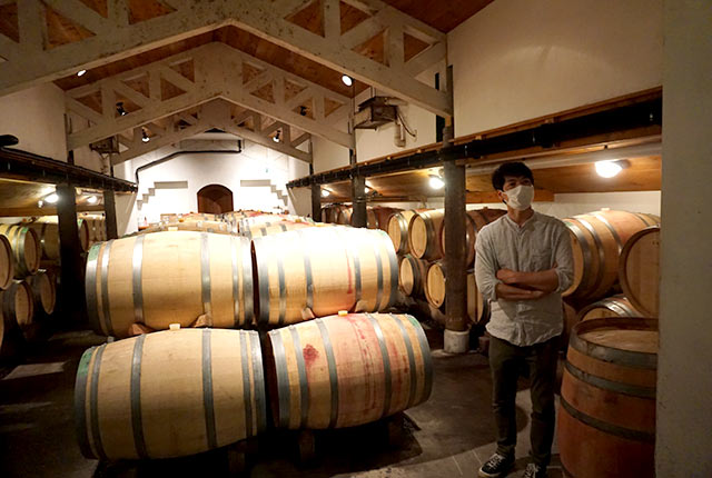 ワイン樽が並ぶ醸造所でインタビューを受ける醸造長・掛川史人さん