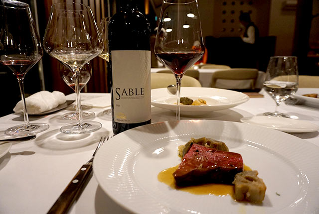 テーブルにサーブされた肉料理と「SABLE（サブル）」が注がれたワイングラス