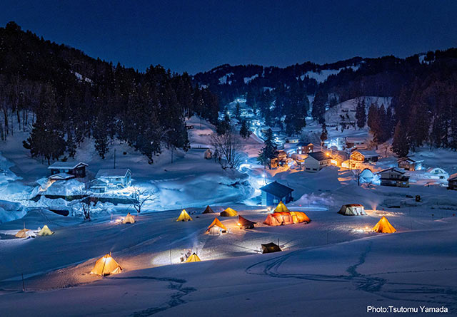夜の雪山でたくさんのキャンプテントがライトアップされている