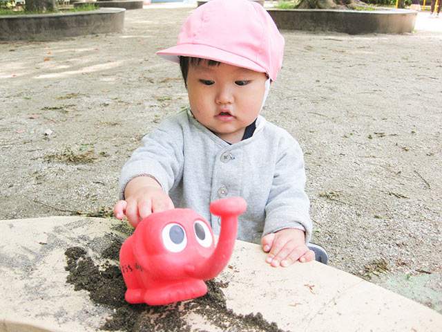 砂場でじょうろを使いながら遊ぶこども