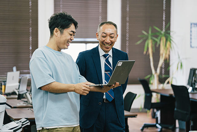 ノートパソコンを手に社長の佐藤さんと談笑する大関さん