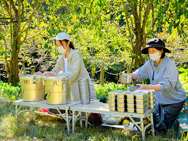 ２人の調理スタッフさんが草むらで昼食を準備している