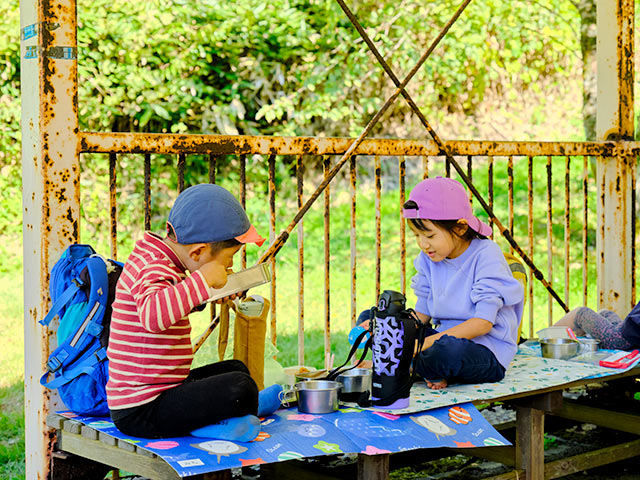 木のベンチに座ってお昼を食べる２人の男の子