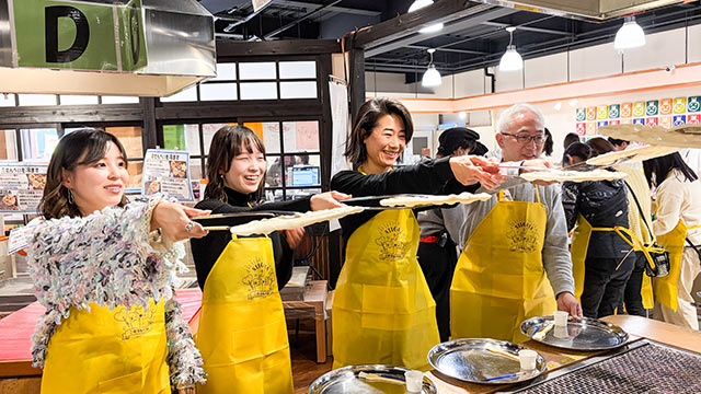 トングで大きなせんべいを持ち上げている参加者たち