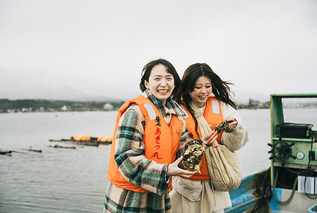 船上で牡蠣を手に笑顔のアリスさんたち