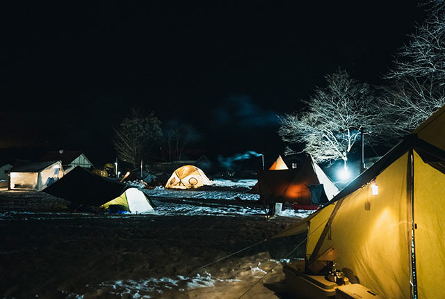 夜の雪上でたくさんのテントに灯りがともっている