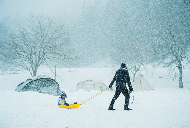 雪が降る中、小さな子がのったソリを引くお父さん