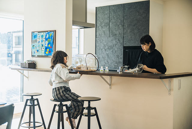 キッチンで家事をする琴絵さんと対面カウンターに座っている娘さん