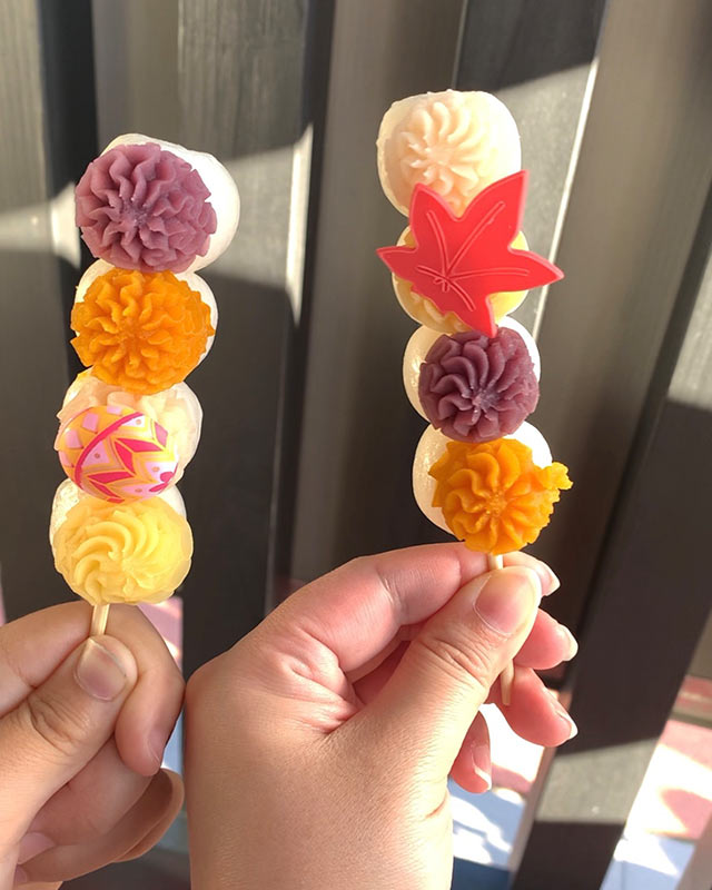 〈弥彦スイーツ〉の「からふる団子」2本を手にしている